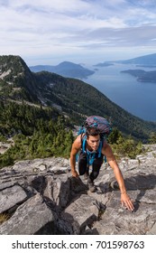 Latin American Male Hiker Is Climbing A Steep Rocky Hill To Get To The Top. Picture Taken On The Way Up To The Lions Mountain In Lions Bay, North Of Vancouver, British Columbia, Canada.