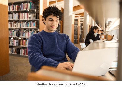 Latin American male student using laptop, focused on working on a diploma project, making researches on internet, studying online in a modern innovation library campus. People. Erudition. Education. - Shutterstock ID 2270918463