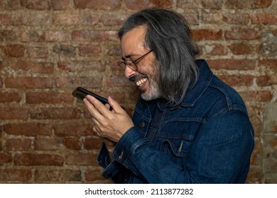 Latin American Man (44) With Long Gray Hair Smiles While Talking On His Cell Phone. Concept Of Technology