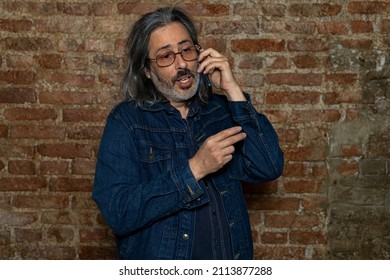 Latin American Man (44) With Long Gray Hair Talking On His Cell Phone. Concept Of Technology