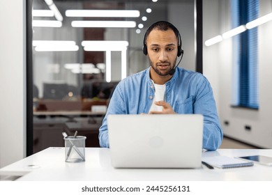 Latin American man in a headset sits in the office in front of a laptop and communicates on a video call. - Powered by Shutterstock