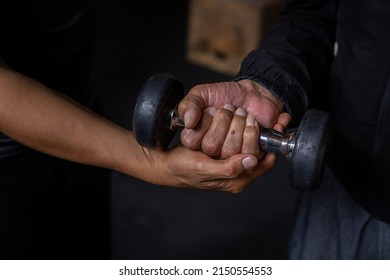 Latin American Senior Male With His Unrecognizable Personal Trainer Do Rehabilitation And Therapy Exercises Holding A Dumbbell In The Gym. Healthy Lifestyle Concept.