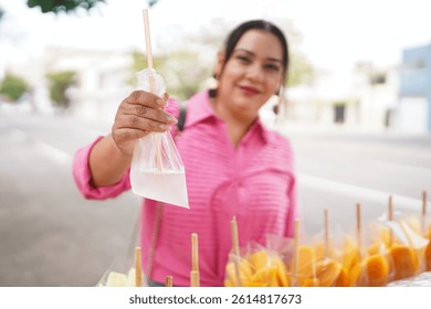 Vendedor callejero estadounidense de Latina sostiene una bolsa de plástico con agua de coco y ofrece fruta fresca en palos en la calle