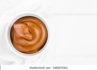 Latin American sweet caramel-like Manjar or Dulce de leche used as spread or filling in baking, photographed on white wood with copy space (Selective Focus, Focus on the top of the cream) 
