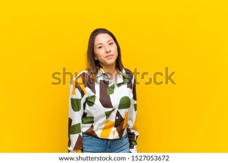 latin american woman with a goofy, crazy, surprised expression, puffing cheeks, feeling stuffed, fat and full of food isolated against yellow wall