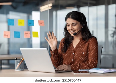 Latin American woman with headset phone using laptop for video call, female online customer support worker waving hand greeting customer, online meeting with colleagues remotely. - Powered by Shutterstock