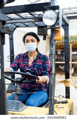 Latin american woman sits in a protective mask behind the wheel of a tractor autocar during a pandemic.
