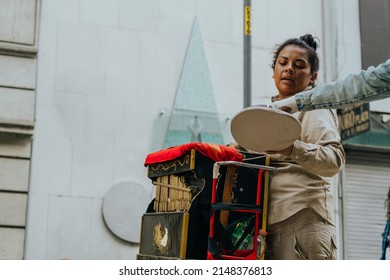 Latin American Woman Working With A Musical Barrel Organ Receiving Money.