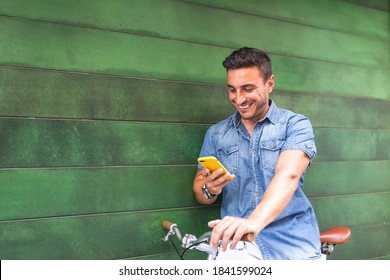 Latin American Young Man Sitting on Bike Using Cellphone . Latino Man Texting on Cellphone in the Street. Lifestyle Concept. - Powered by Shutterstock