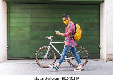 Latin American Young Man Wearing Mask and Using Phone Outdoors. Latino Man Holding Bike in the Street. Lifestyle Concept.