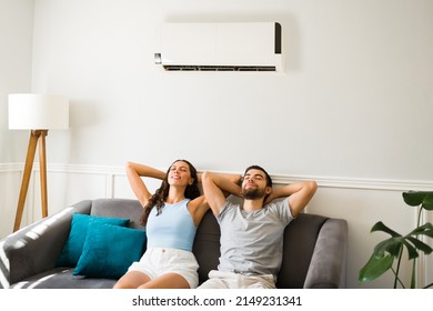 Latin attractive couple relaxing and resting on the couch with the air conditioner on during a hot summer  - Shutterstock ID 2149231341