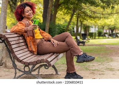 Latin Black Woman With Mobile Phone On Bench Sitting In Autumn