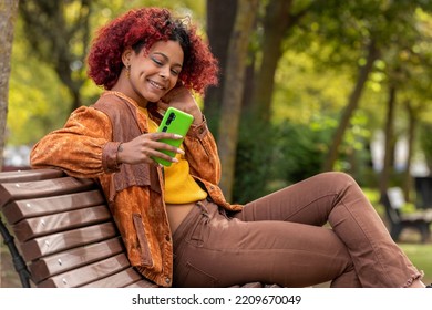 Latin Black Woman With Mobile Phone On Bench Sitting In Autumn