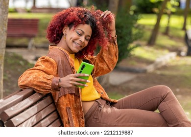 Latin Black Woman With Mobile Phone On Bench Sitting In Autumn