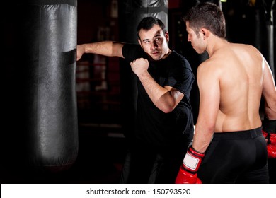 Latin Boxer and his coach practicing some moves on a punching bag at a gym - Powered by Shutterstock