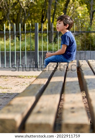 latin boy sitting in profile waiting on a square bench. vertical