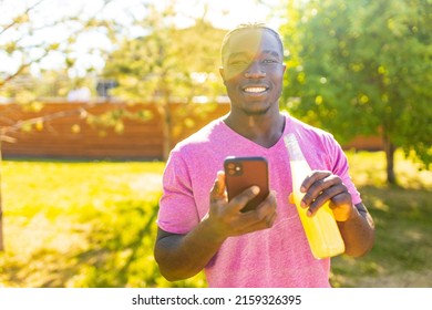 latin brazilian man drinking fresh cold lemonade in hot summer day in sunny park and holding smartphone