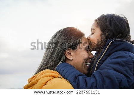 Latin child kissing her mother outdoor during winter time - Focus on mom face