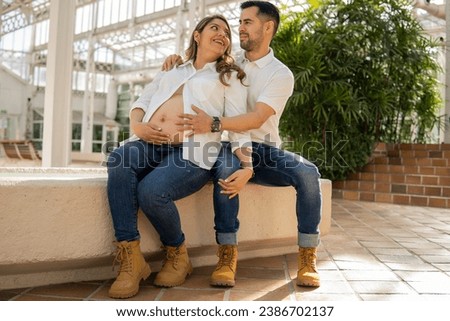 Latin couple expecting a baby sitting next to a fountain looking at each other with love
