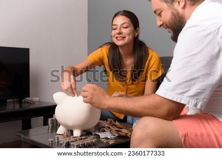 Latin couple keeps their saved money in a piggy bank at home. Couple savings concept