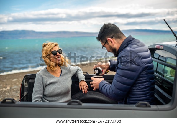 Latin couple laugh and drink yerba mate in the\
open air against the backdrop of the lake. Patagonian landscape.\
Spending time together, tradicional drinks in South America,\
friendship. love concept