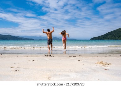 Latin Couple Running Towards The White Sand Beach And Blue Sea, Anchieta Island In Brazil  Brasil Ilha