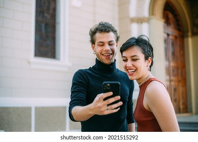 Latin Couple Walking In City Using Smartphone Outdoors.