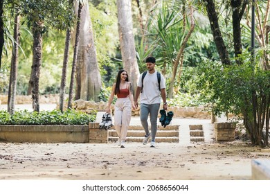 Latin Couple Walking In A Park With Roller Skates In Hand