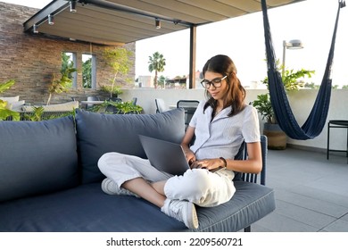 Latin Ethnic Woman Working On Her Laptop Sitting On A Sofa From A Hotel Penthouse At Sunset