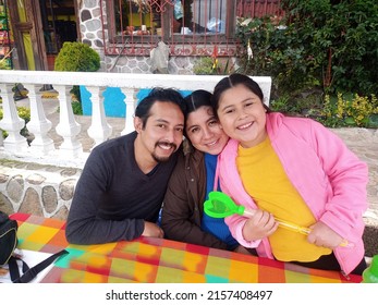 Latin Family Of Dad, Mom And Daughter Enjoy A Picnic Flying A Kite And Jumping With Happiness For Vacations And Days Off Celebrating Their Love And Quality Time Without A Cell Phone
