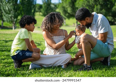 Latin family of mother, father, 7 year old son and baby together in a park dressing the baby on a sunny day - Powered by Shutterstock