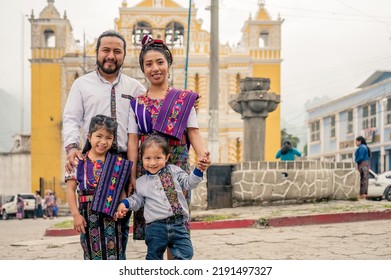 Latin Family Smiling Looking At The Camera With Their Two Children.
Hispanic Family In Front Of A Church In A Rural Area.