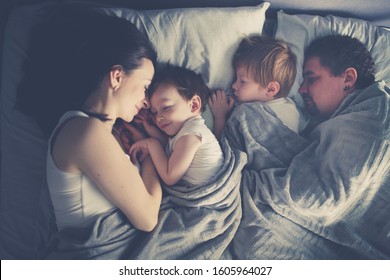 Latin family with two children sleeping in bed, top view. Children between parents. Happy childhood and parenthood concept. Children in the morning come to their parents' bedroom