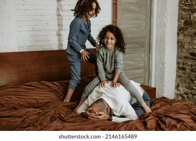 Latin Father And Children Jumping On Bed And Laughing While Playing Together At Home In Mexico Latin America