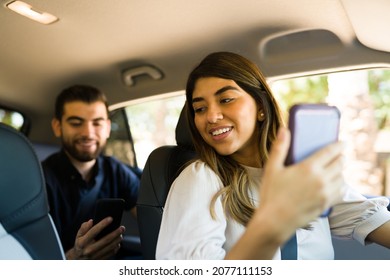 Latin Female Driver Talking With A Man In The Back Seat While Driving. Passenger Using A Carpool Service App 