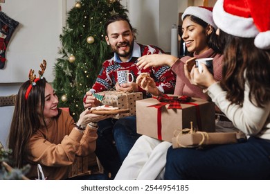 Latin friends holding gifts and sitting near Christmas tree at home in Mexico. Holidays and celebration in Latin America - Powered by Shutterstock