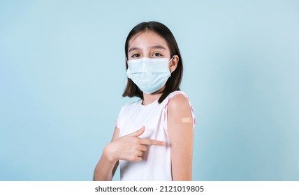 Latin Girl Child Wearing Face Mask After Getting A Vaccine Protection The Coronavirus And Showing Arm With Bandage After Receiving Vaccination On Blue Background