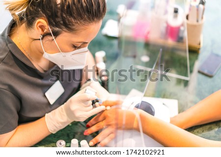 Latin girl with face mask painting colorful nails of the client. Reopening after the corod-19 pandemic. Manicure and Pedicure Salon. Coronavirus