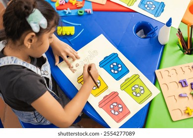 Latin girl in a primary school classroom, writing and painting the word "Recycle." Waste separation bins are visible as she learns about recycling - Powered by Shutterstock - Get 15% off with code: PIKWIZARD15