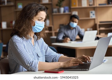 Latin girl student wearing face mask studying on laptop. Hispanic professional woman employee in facemask working sitting at table in modern office coworking space keeping safe social distance. - Powered by Shutterstock