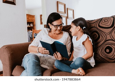 latin grandmother with granddaughter sitting on couch at home and reading book in Mexico city - Powered by Shutterstock