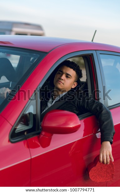 Latin guy stuck in traffic holding a heart outside of\
the car