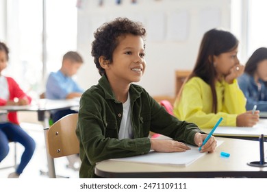 Latin guy writes in exercise notebook and listening teacher, taking notes or writing test. Group of children working diligently and learning - Powered by Shutterstock