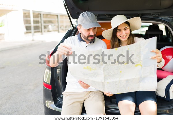 Latin handsome\
man and young woman smiling while looking at a big map to plan a\
route for their family road trip\

