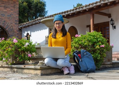 Latin Hipster Woman Sitting In A Main Square With A Laptop On Her Lap And Looking Straight At The Camera