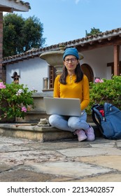 Latin Hipster Woman Sitting In A Small Central Square With A Laptop On Her Lap And Looking Straight At The Camera