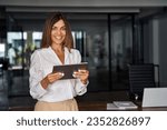 Latin Hispanic 40s years mature business woman looking at camera. smiling European businesswoman CEO holding digital tablet using fintech tab online application standing in modern office, copy space