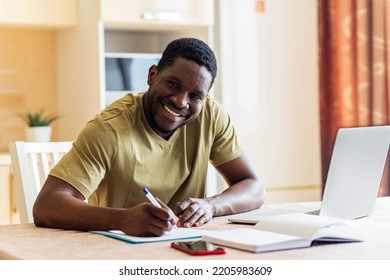 Latin Hispanic Man Looking Happy While Sitting With Laptop And Papers At Kitchen