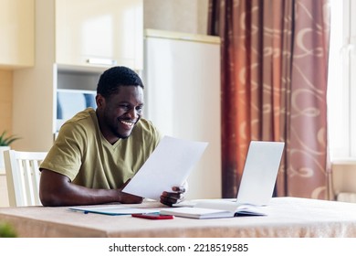 Latin Hispanic Man Looking Happy While Sitting With Laptop And Papers At Kitchen