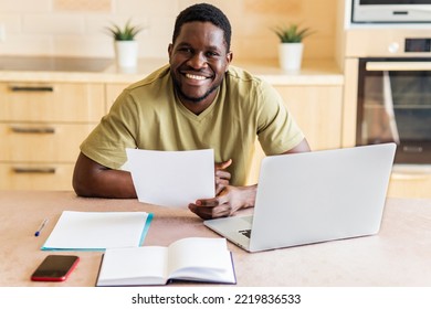 Latin Hispanic Man Looking Happy While Sitting With Laptop And Papers At Kitchen